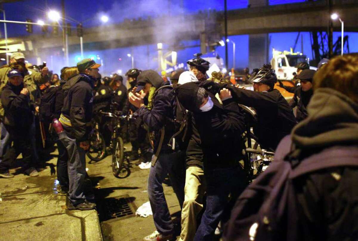 Police scuffle with protesters after deploying two flash-bang grenades on Monday, December 12, 2011 at the Port of Seattle. Hundreds of anti-Wall Street protesters gathered at the port and tried to shut down operations. Protesters scuffled with police during the rally and police used pepper spray and two flash-bang grenades to disperse the crowd after a protester threw a lit road flare toward officers. Another threw red paint on officers.