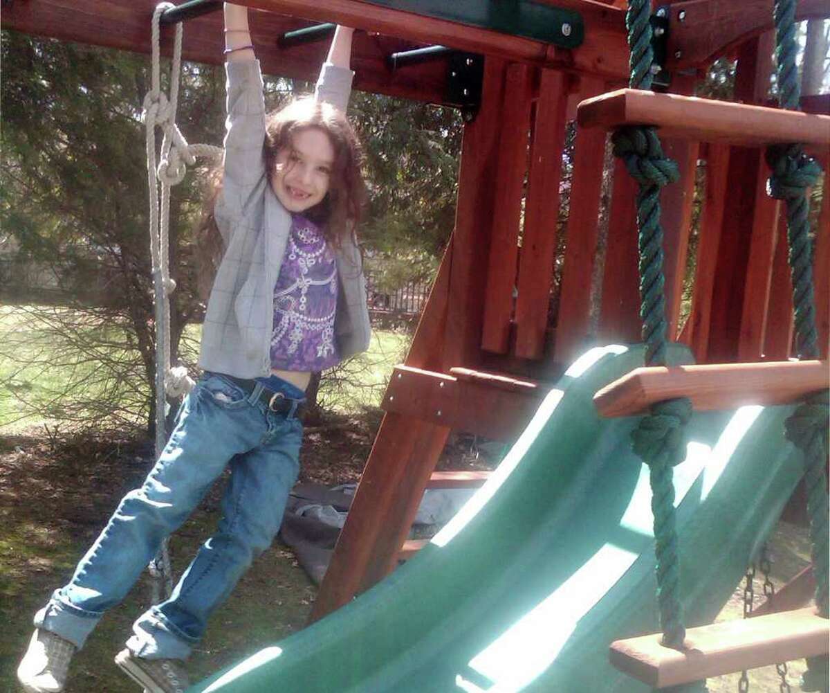 Lynnea Moskowitz, daughter of Cary Moskowitz, hangs out on the monkey bars of her swing set in her Sturges Highway yard. The Zoning Board of Appeals on Tuesday approved a stipulated judgment designed to settle a dispute over the swing set's location.