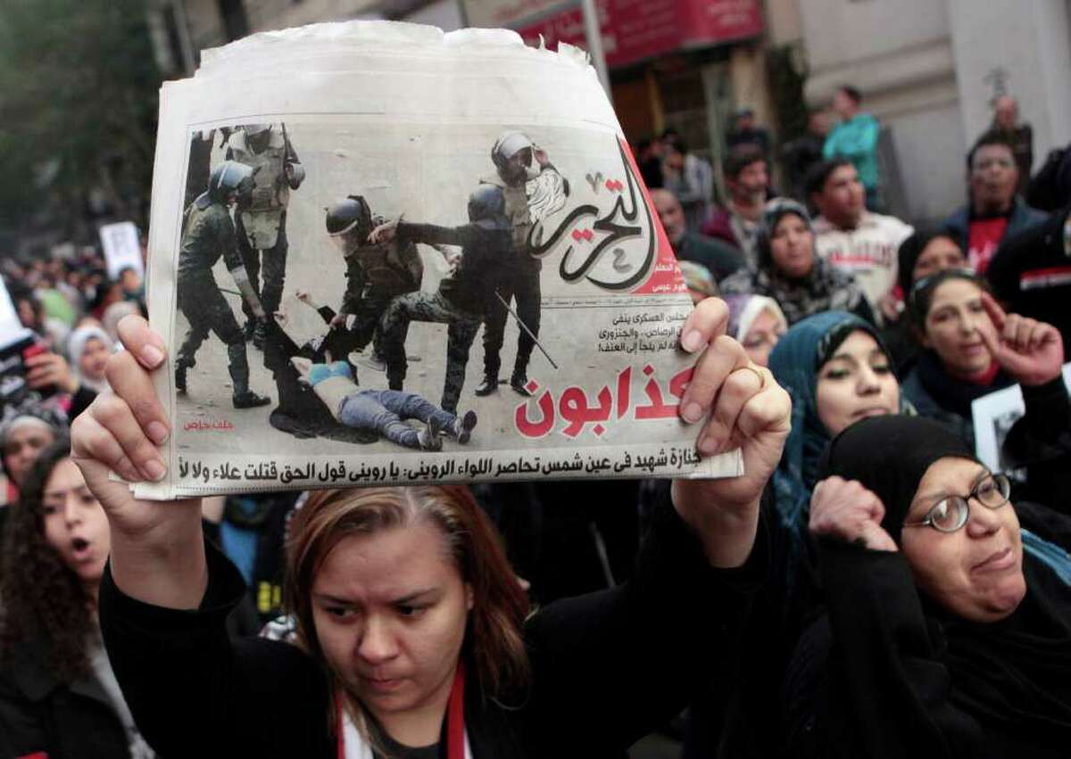 AMR NABIL : ASSOCIATED PRESS CATALYST: An Egyptian woman raises a copy of Al Tahrir newspaper, which published a now-famous picture of soldiers beating a woman with batons and ripping away her abaya to reveal her blue bra before one plants his boot on her chest. Thousands of women marched in Cairo streets Tuesday in what may have been the biggest women's demonstration ever in Egypt.