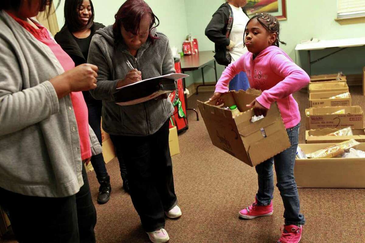 Nivea Shelton, 8, holds a box of food for her family including her mother, Veronica McCurtis, far left, while Pamela Moore, center/left, signs for her box of food with a member of Lively Stone Church Food Ministry, Barbara Gay, left, as the ministry holds a food distribution with the Merced Housing Texas program at Artisan at Willow Springs apartments in San Antonio on Saturday, Dec. 17, 2011.