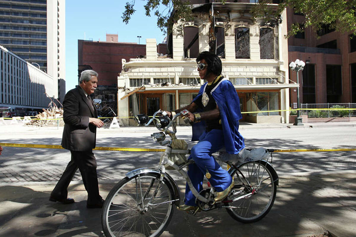 An Elvis impersonator rides by as pedestrians, bikers and others hang out at Main Plaza to watch the remains of the Wolfson Building across the street on East Commerce, Sunday, Oct. 2, 2011. The building, built in 1880, was destroyed in a four-alarm fire that started Saturday morning.