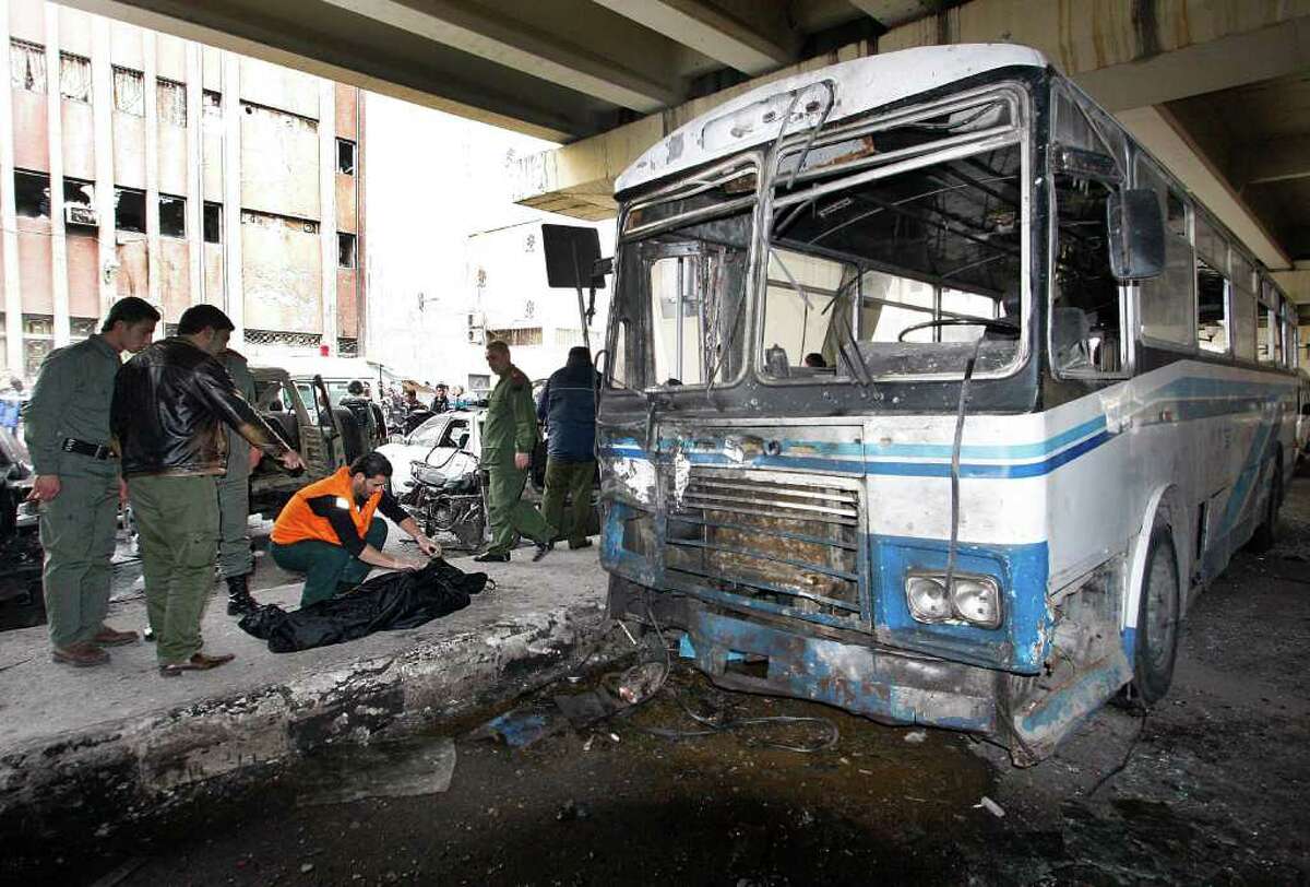 Two Syrian security men, left, look to a civil defense worker as he checks a dead body, next to a damaged riot police forces bus at the scene of a suicide bomb attack, at Midan neighborhood, in Damascus, Syria, on Friday Jan. 6, 2012. An explosion ripped through a police bus in the center of Syria's capital Friday, killing many in an attack authorities blamed on a suicide bomber, an official and state-run TV said. (AP Photo/Muzaffar Salman)