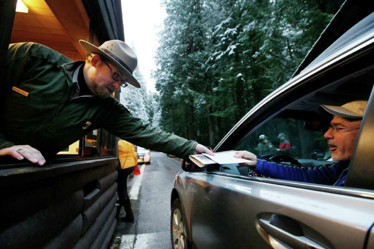 Mount Rainier National Park Ranger Matt Chalup, left, hands park information to one of the first visitors to the park at the Nisqually entrance Saturday morning, Jan. 7, 2012, near Ashford, Wash. The park opened for the first time since the shooting death of Ranger Margaret Anderson on Jan. 1. A memorial service for Anderson will be Tuesday, Jan. 10, in Tacoma, Wash. (AP Photo/Elaine Thompson)