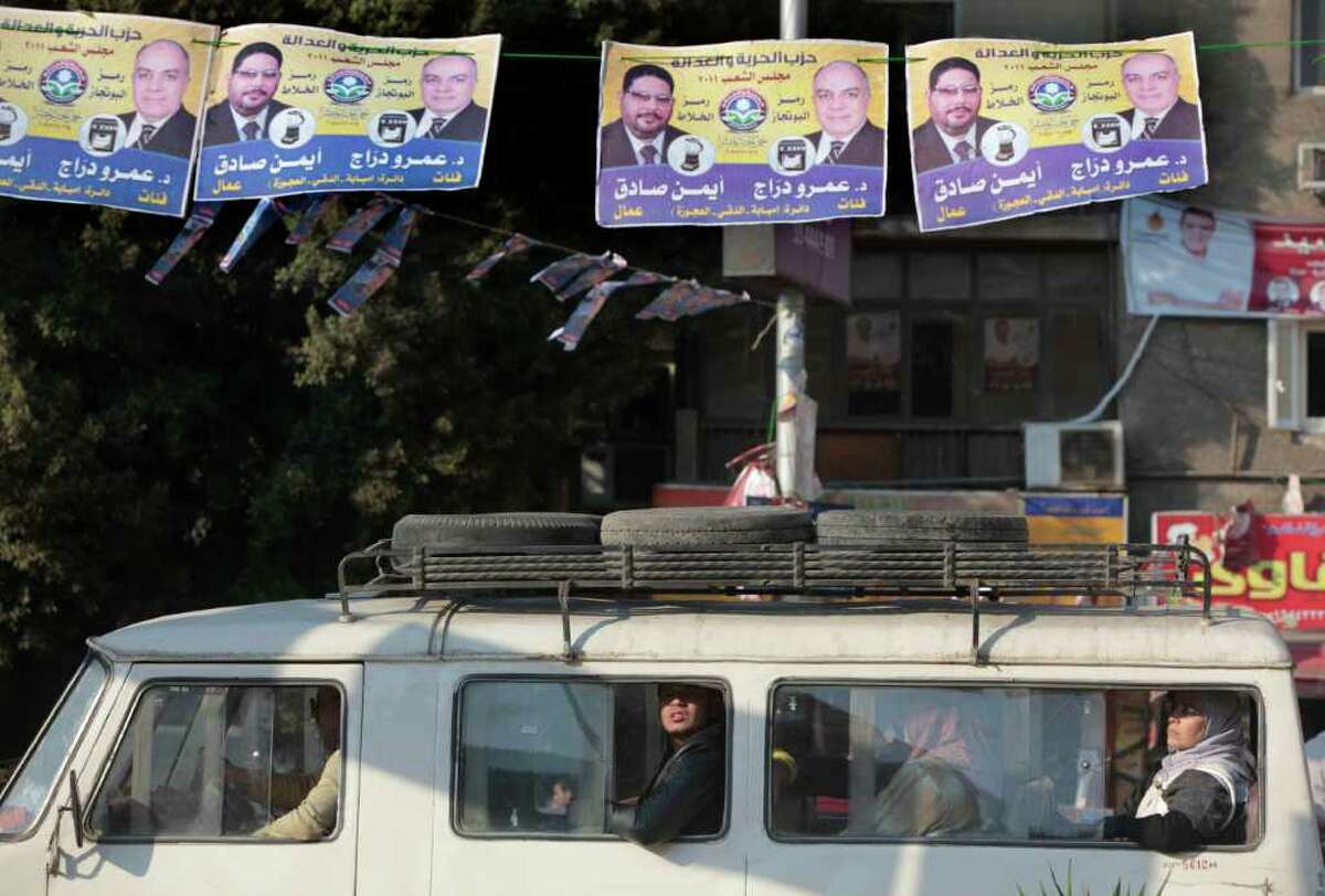 FILE - In this Monday, Dec. 12, 2011 file photo, Egyptians in a minibus pass under electoral posters with pictures of candidates from the Muslim Brotherhood's Freedom and Justice Party, and Arabic that reads, "Ayman Sadek and Amr Drag," in Cairo, Egypt. The Muslim Brotherhood has emerged as the biggest winner in parliamentary elections, but the fundamentalist group that has long dreamed of ruling Egypt is likely to be cautious about flexing its newfound muscle. (AP Photo/Amr Nabil, File)