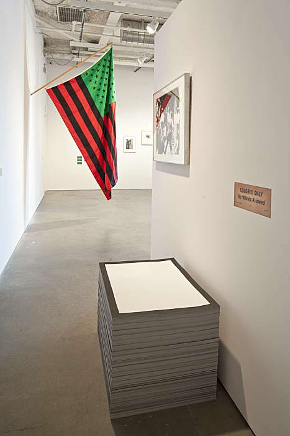 INstallation view of "Huckleberry Finn" exhibition at CCA showing "Untitled (The End)" (1990) lithograph in unlimited edition by Felix Gonzalez-Torres, "Birmingham Race Riot" (1964) screenprint by Andy Warhol and "African-American Flag" (1990) dyed fabric by David Hammons.