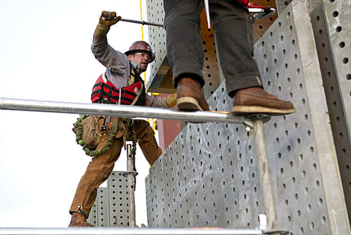 Ironworkers work on the Bay Bridge Self-Anchored Suspension Span as a piece of the tower for the new bridge is lowered into place at the construction site in San Francisco, Calif., on Monday, February 28, 2011.