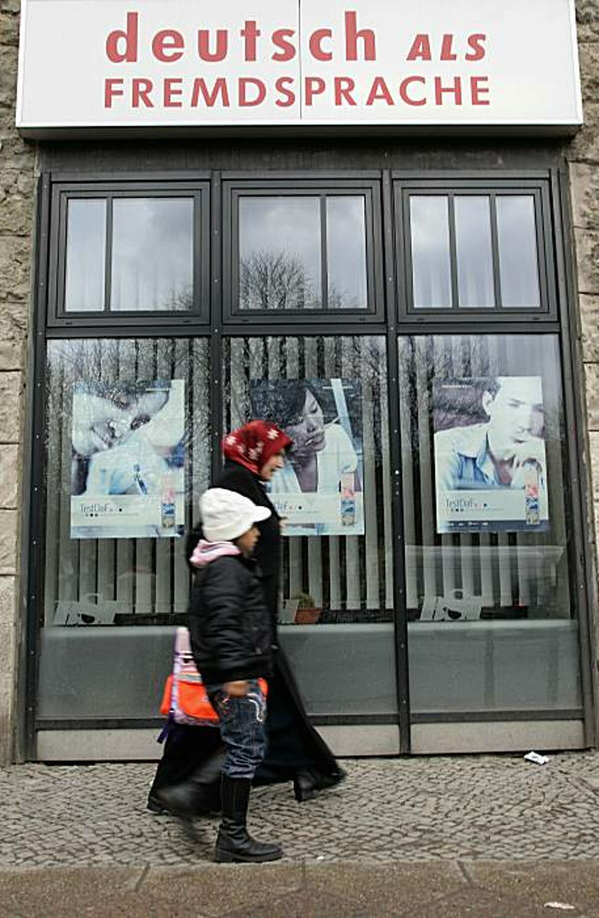 BERLIN, GERMANY - JANUARY 27: A muslim woman wearing a headscarf and her child walk past a sign of a language school that reads 'German as foreign language' in the immigrant-heavy district of Kreuzberg on January 27, 2011 in Berlin, Germany. German politicians are debating past and future govenment policies to encourage the integration of immigrants into German society, a debate that was most recently sparked by a controversial book by German Social Democrat (SPD) Thilo Sarrazin, in which he accuses Muslims of being more reluctant to integrate than other immigrant groups.