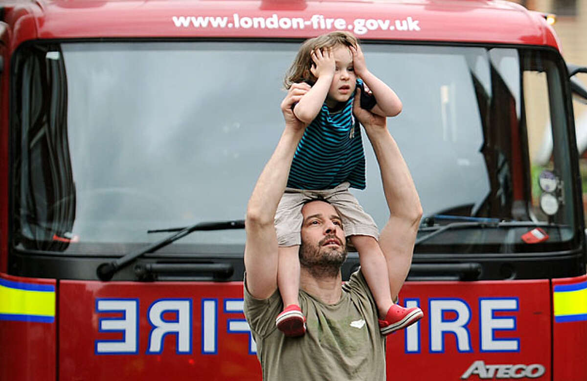 A man holds a child on his shoulders to watch firemen tackling a rooftop blaze on a roof above an apartment in London on May 19, 2010. The building was extensively damaged but no one was injured.