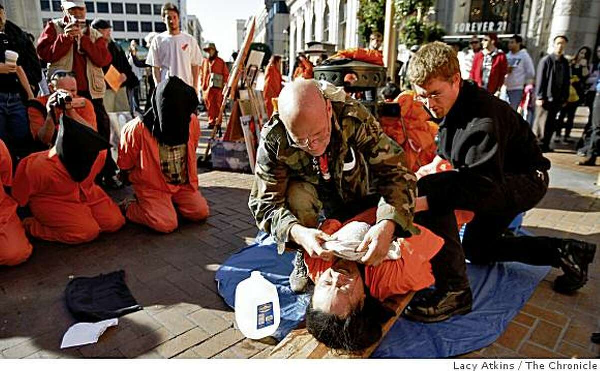 Michael Dean( left) holds Noel Juan down and simulates water boarding at a protest marking the 7th anniversary onf the U.S. interrogation of prisoners in Guantanamo Bay, Sunday Jan. 11, 2009, in San Francisco, Calif.