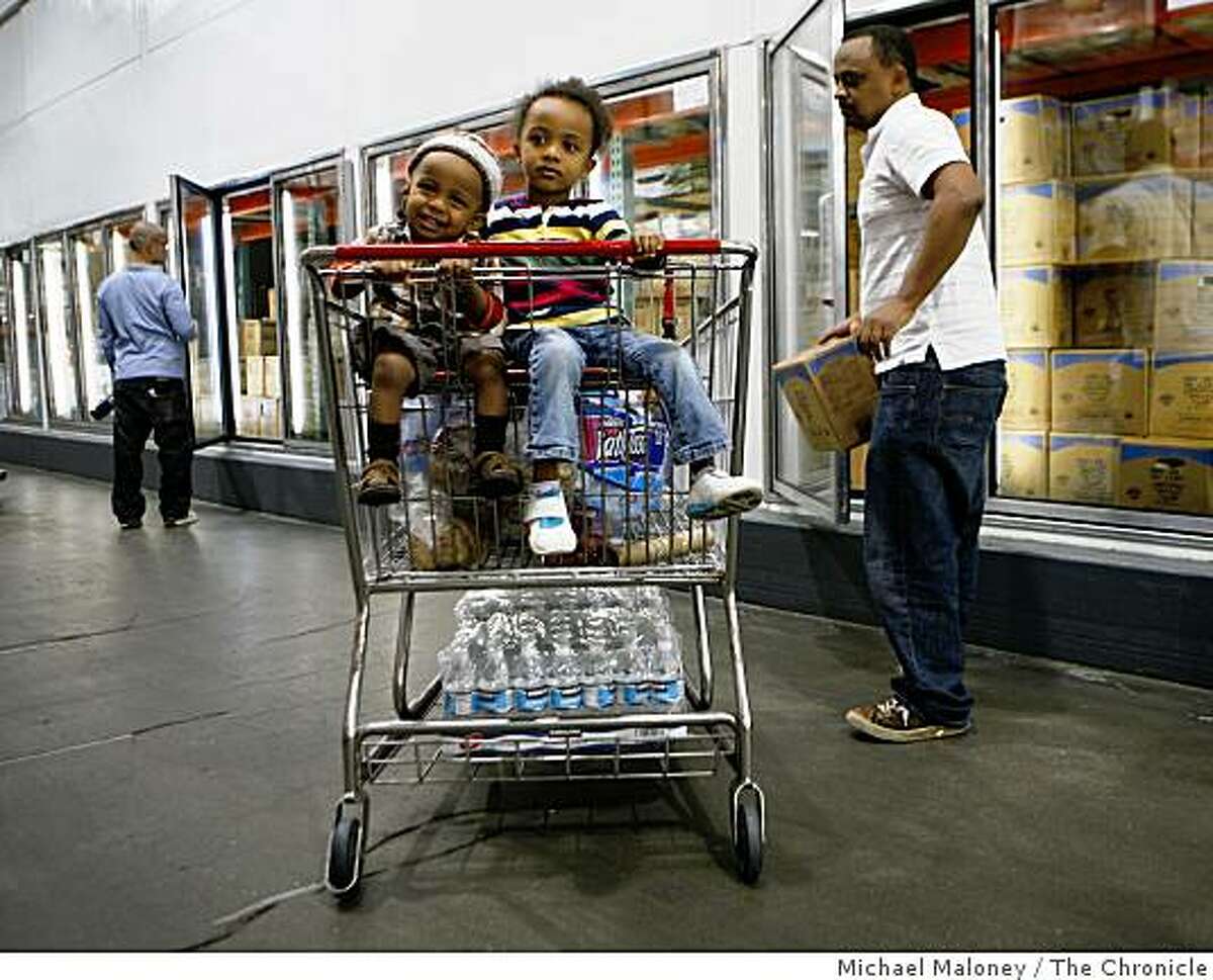 Jonah, left, and Liya get a ride in the grocery cart at the San Francisco Costco as their dad Fasil Fikreab, right, does the family grocery shopping.