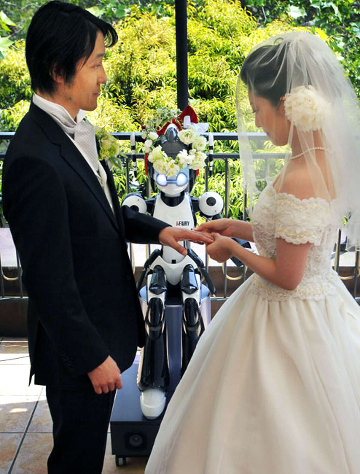 Bride Satoko Inouye, 36, puts a ring on a finger of her groom Tomohiro Shibata 42, as I-Fairy, a four-foot tall seated robot, wearing a wreath of flowers, directs their wedding ceremony at a Tokyo restaurant Sunday, May 16, 2010. The wedding was the firsttime a marriage had been led by a robot, according to manufacturer Kokoro Co.