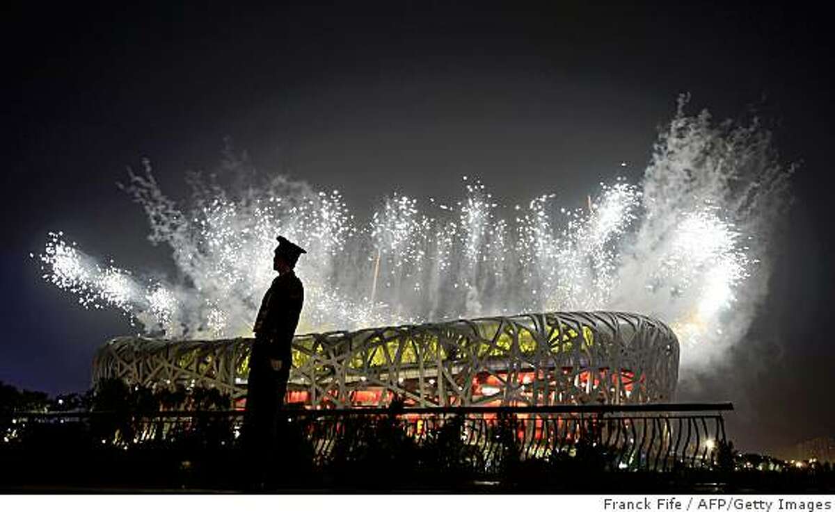 A Chinese security personnel stands guard as fireworks display light up above the National Stadium also known as the "Bird's Nest" during the closing ceremony of the 2008 Beijing Olympic Games on August 24, 2008.