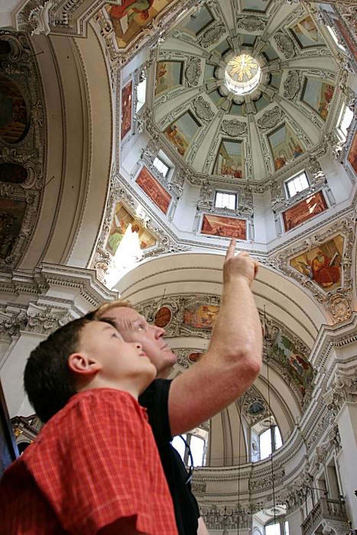 A father and his son gaze at the Salzburg Cathedral dome which has ceiling paintings depicting the life of Christ.