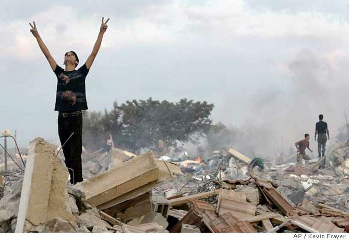 A Palestinian man celebrates in the rubble of demolished houses in the former Jewish settlement of Netzarim, early Monday, Sept. 12, 2005. Thousands of triumphant Palestinians poured into abandoned Jewish settlements early Monday, setting empty synagogues on fire and shooting in the air, as the last Israeli soldier left the Gaza Strip, completing Israel's pullout after 38 years of occupation. (AP Photo/Kevin Frayer)