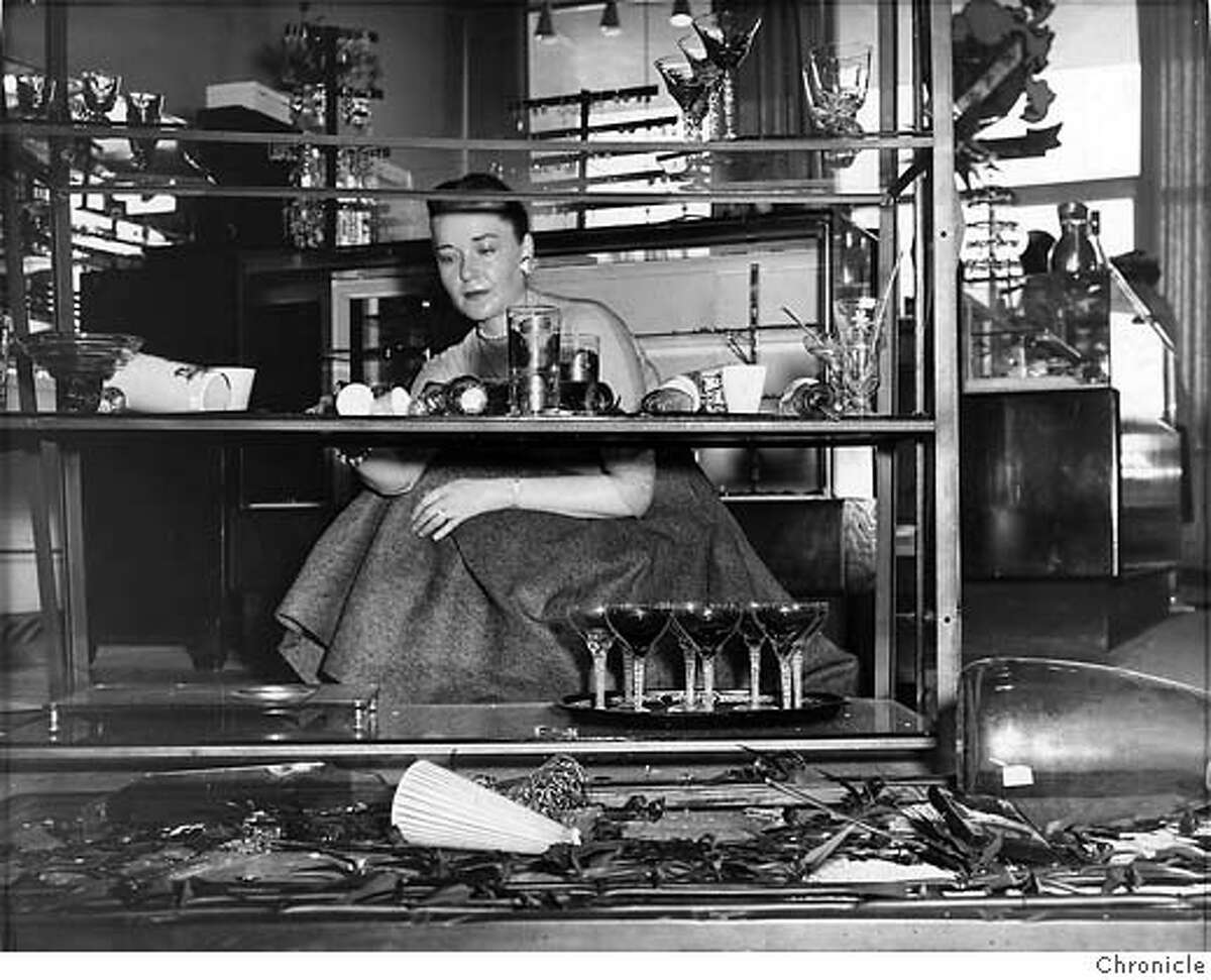 Margaret Gaines began to tidy up the debris of broken glassware at a Stonestown shop following the earthquake in March 1957