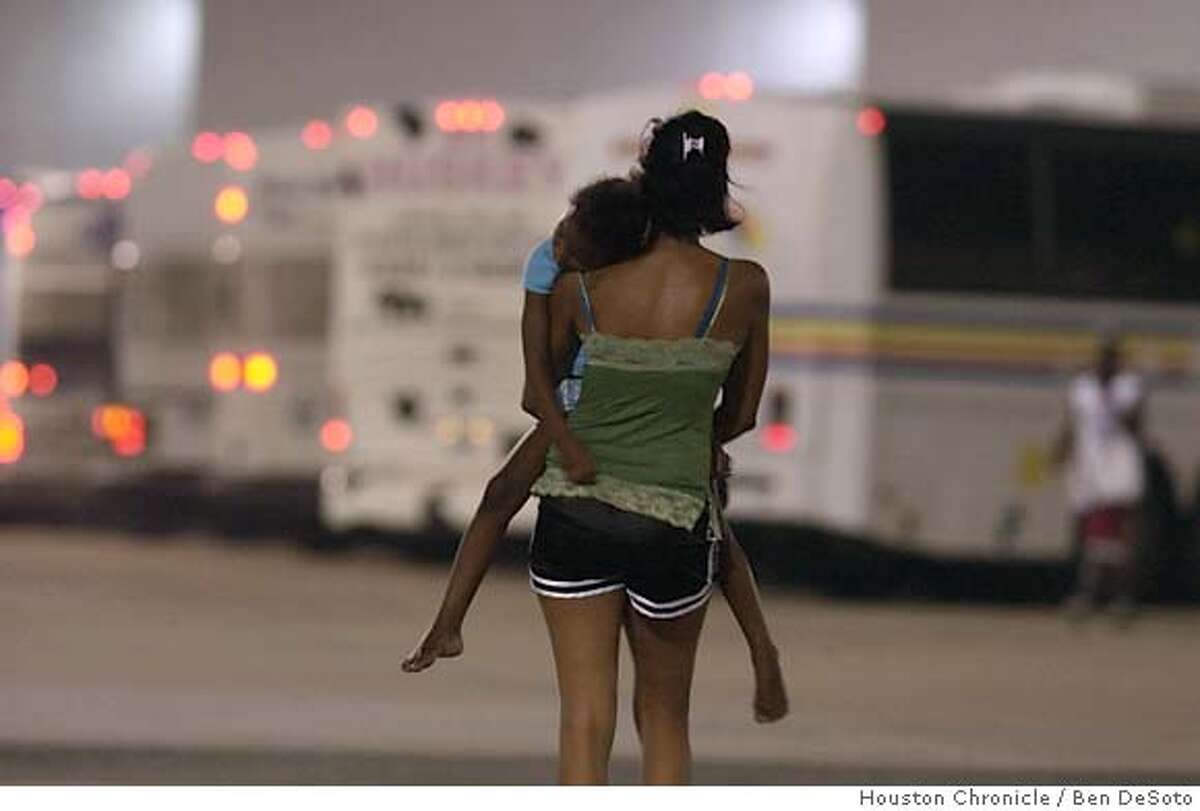 A woman carries a child the final distance to an eventual night's rest after a day's journey from New Orleans to Houston. A decision to close Houston's Reliant Park to incoming refugees was reversed about 1 am Friday morning Sept. 2, 2005. About 50 buses, averaging 50 passengers each, were allowed into the complex and officials began converting The Reliant Center building into an intake area. Those refugees, mostly from the New Orleans SuperDome, might be relocated in the coming days to cities as far as Dallas, Texas. (AP Photo/Ben DeSoto/Houston Chronicle)