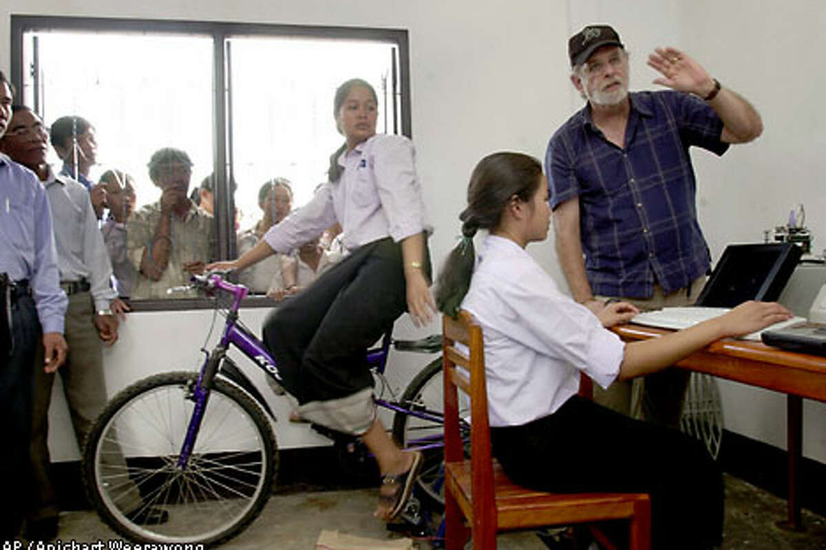 Lee Thorn, right, a Vietnam veteran and founder of San Francisco's Jhai Foundation, explains to Laotian schoolgirls how the world's first wireless, bicycle-powered PC will operate. Associated Press photo by Apichart Weerawong