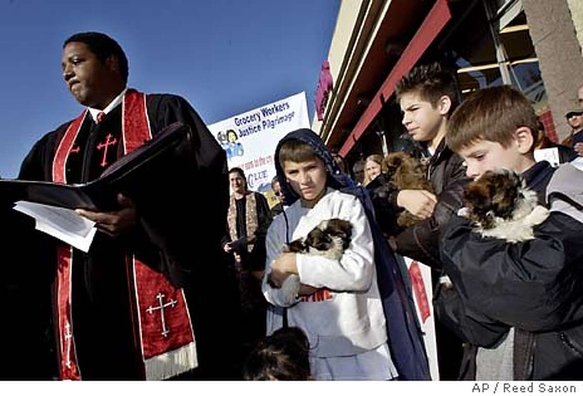 Glen Colson, 11, center, and his brothers Mark, 12, and Jonathan, 8, right, hold puppies as Pastor Palmerdon Palmer Jr. offers a blessing for the group at a sendoff rally for workers traveling to the Northern California home of Safeway CEO Steve Burd, at a Pavilions store in Los Angeles' Sherman Oaks neighborhood Tuesday, Jan. 27, 2004. Other workers were to join the group in Ventura and San Jose en route to hold a prayer vigil outside Burd's home in Alamo in the East Bay area in an effort to get talks in the four-month-old strike started again. The group said Burd is known for his philanthropy toward dogs. (AP Photo/Reed Saxon)
