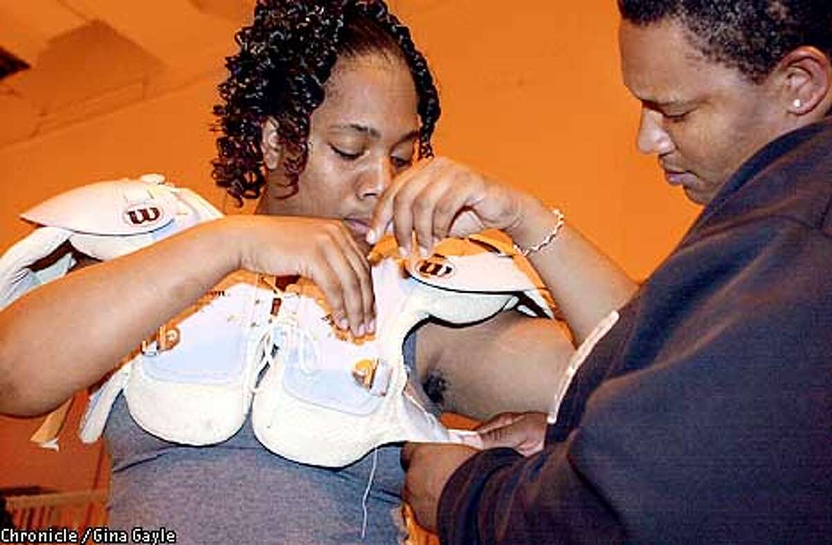 Monique Cook (L) is helped by Michelle Mitchell putting on her pads for a recent practice the SF Tsunami WAFL football team had at McClymonds High School. Photo by Gina Gayle/The SF Chronicle.