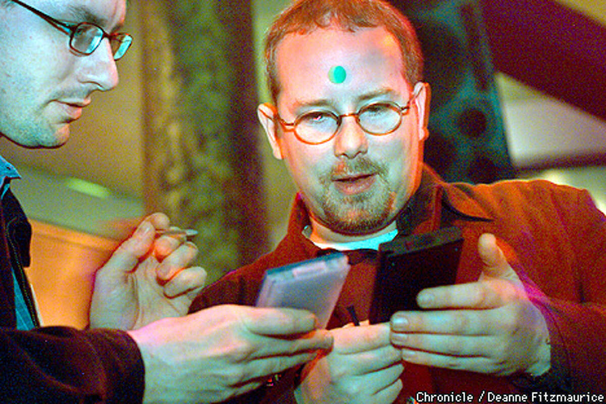 Jeremy Reid, SF, a corporate recruiter for Digital Island wears a green dot on his forehead to signify that he is recruiting and at left, Mike Coulson wearing a red dot (out of view) is looking to see that his resume was successfully beamed to Reid's palm pilot via his own palm pilot. Coulson is looking for work in product management. They are at a Pink Slip party at Club NV in San Francisco's South of Market area. CHRONICLE PHOTO BY DEANNE FITZMAURICE