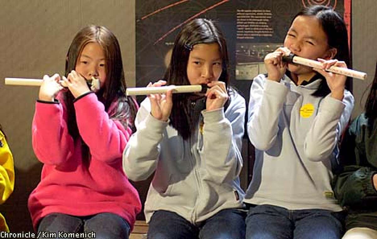West Portal Elementary School fifth-graders Karen Chu, Liana Huang, and Elaine Quan played the membraneophone, an instrument made of plastic pipe and surgical glove pieces, at a Public Science Day event. Chronicle photo by Kim Komenich