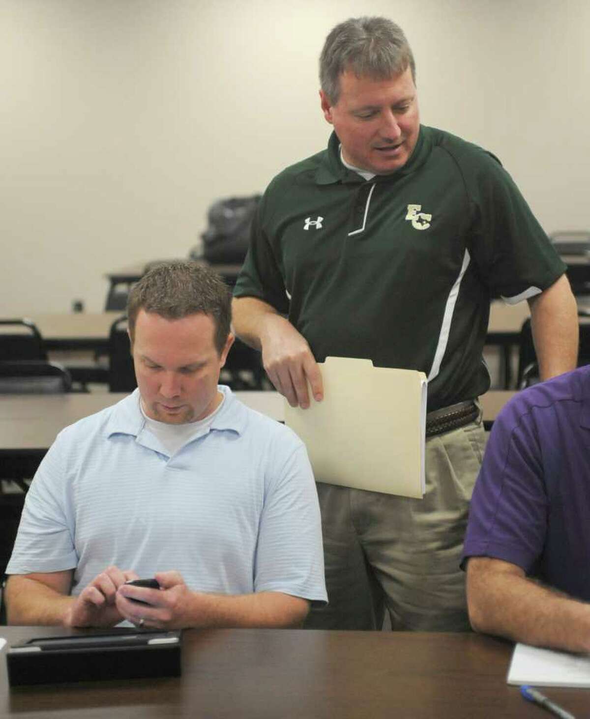 Daniel Andrews, left, with East Chambers, sends a text as Russ Sutherland, right, of East Chambers talks with others at the table. The high school sports realignment from the UIL was released at 9:00 am Thursday morning. Coaches from the area gathered at the Region 5 education service center in Beaumont for the release of the districts and to plan scheduling of games for next season. Dave Ryan/The Enterprise
