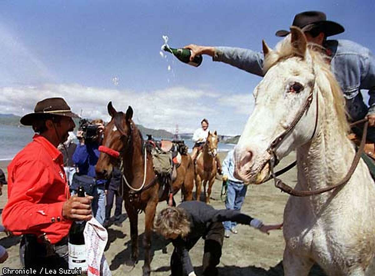 Ray Piecuch is doused with champagne by Keith Simon of Woodside, riding his horse Howard, after finishing his cross country trek ending at Baker Beach on Sunday afternoon. Bo, Piecuch's horse who made the cross country trek with Piecuch, is in background with red nose band. Photo By Lea Suzuki