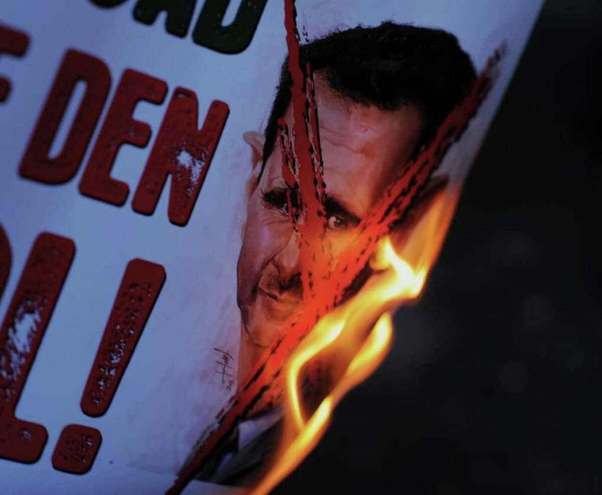 Protesters set on fire a placard in Turkish that reads " Assasin Assad, get out of Syria" as dozens of Syrians living in Turkey and human right activists stage a protest outside the Syrian consulate to condemn the latest killings in Syria, in Istanbul, Turkey, Saturday. (AP Photo)