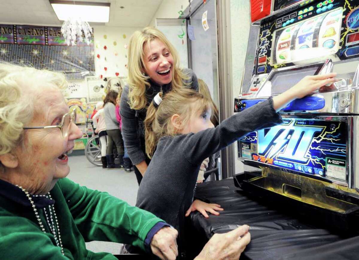 Junior League of Greenwich member Jennifer Stranzl laughs as she watches her daughter, Chloe, 4, place a coin in a slot machine for Nathaniel Witherell resident Mary Klein, left, during the third annual Casino Party hosted by The Junior League of Greenwich at the Nathaniel Witherell nursing home in Greenwich, Saturday afternoon, Feb. 4, 2012.