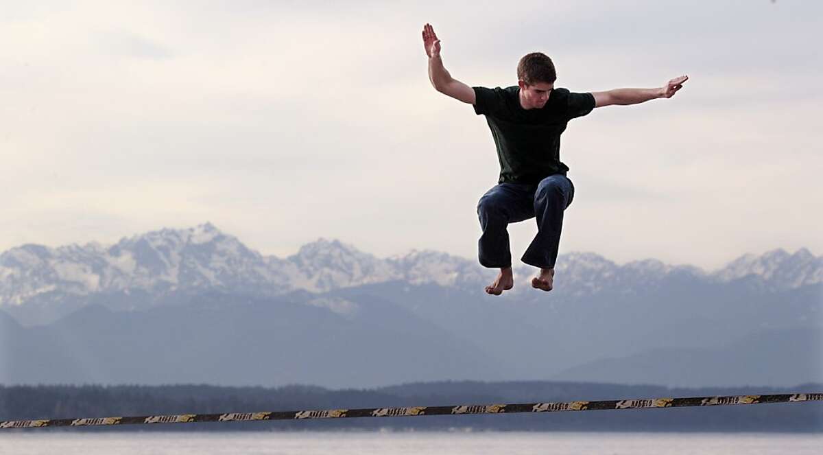 Bryce Beblavi leaps above a slackline of nylon webbing anchored between posts and in view of the Olympic Mountains in Golden Gardens park Tuesday, Feb. 7, 2012, in Seattle. After several days of sun and temperatures hitting near 60 degrees, a few showers and slightly cooler temperatures are predicted for the Puget Sound region. (AP Photo/Elaine Thompson)