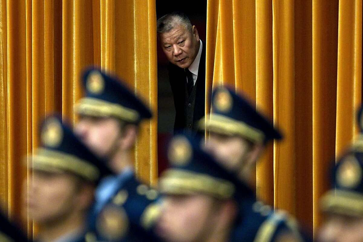 A man peeks through curtains while members of an honor guard, front, stand ready before a welcoming ceremony for Canadian Prime Minister Stephen Harper at the Great Hall of the People in Beijing Wednesday, Feb. 8, 2012. (AP Photo/Alexander F. Yuan)