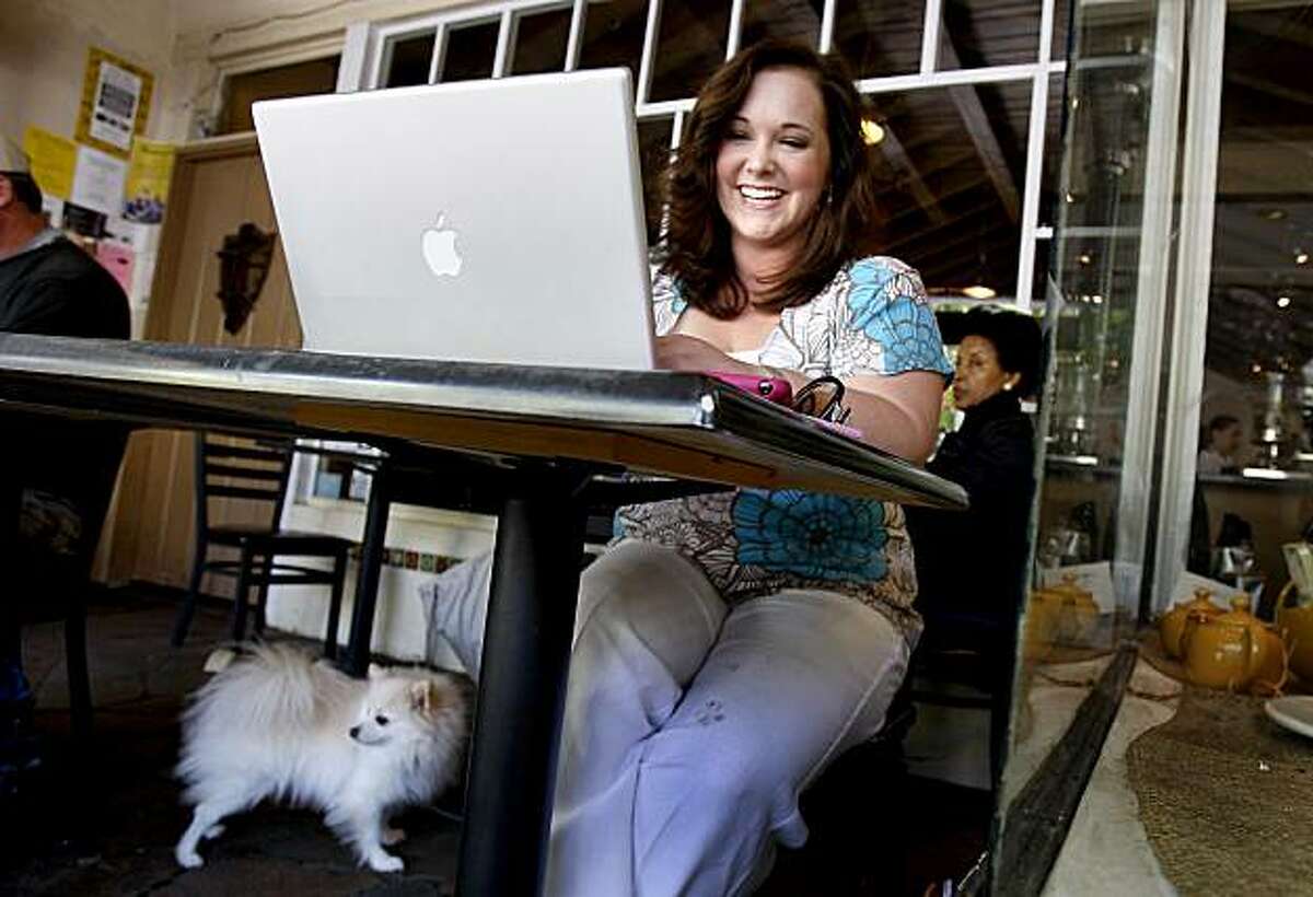 Lauren Bernsen laughs as she reads an email while working on her iPhone application at an outdoor cafe in downtown Palo Alto Thursday April 16, 2009. Her dog, Monte, waits nearby. The iPhone has attracted plenty of developers and programmers, but the alure of the platform even extends to people with no programming background at all.