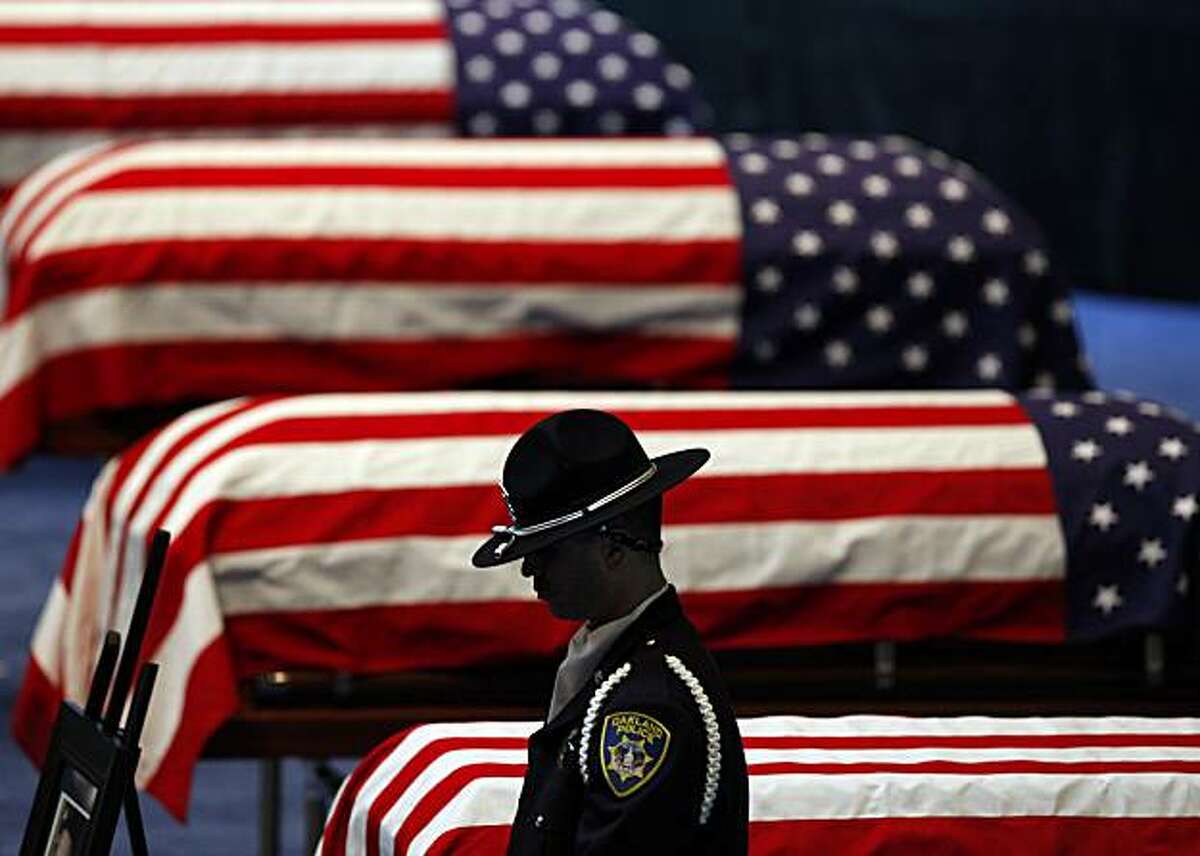 An Oakland Police honor guard stands his post next to the flag-draped caskets of Oakland Police Officers Sgt. Mark Dunakin, 40; John Hege, 41; Sgt. Ervin Romans, 43; and Sgt. Daniel Sakai, 35, are carried by law enforcement officers into Oracle Arena on Friday, Mar. 27, 2009, in Oakland, Calif. Thousands of officers and firefighters from around the nation and overseas along with mourners turned out for Friday's funeral for the four veterans. The four officers were shot in the line of duty Saturday, March 21. (Michael Macor/ San Francisco Chronicle, Pool)