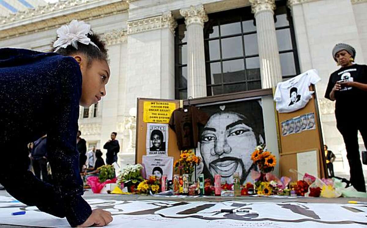 Joyous Miralle DeAsis, 8, of Oakland writes a message on a banner next to a memorial for Oscar Grant as people gather in front of Oakland City Hall on Friday after a judge sentenced former BART police officer Johannes Mehserle to two years in prison for the January 2009 death of Grant.