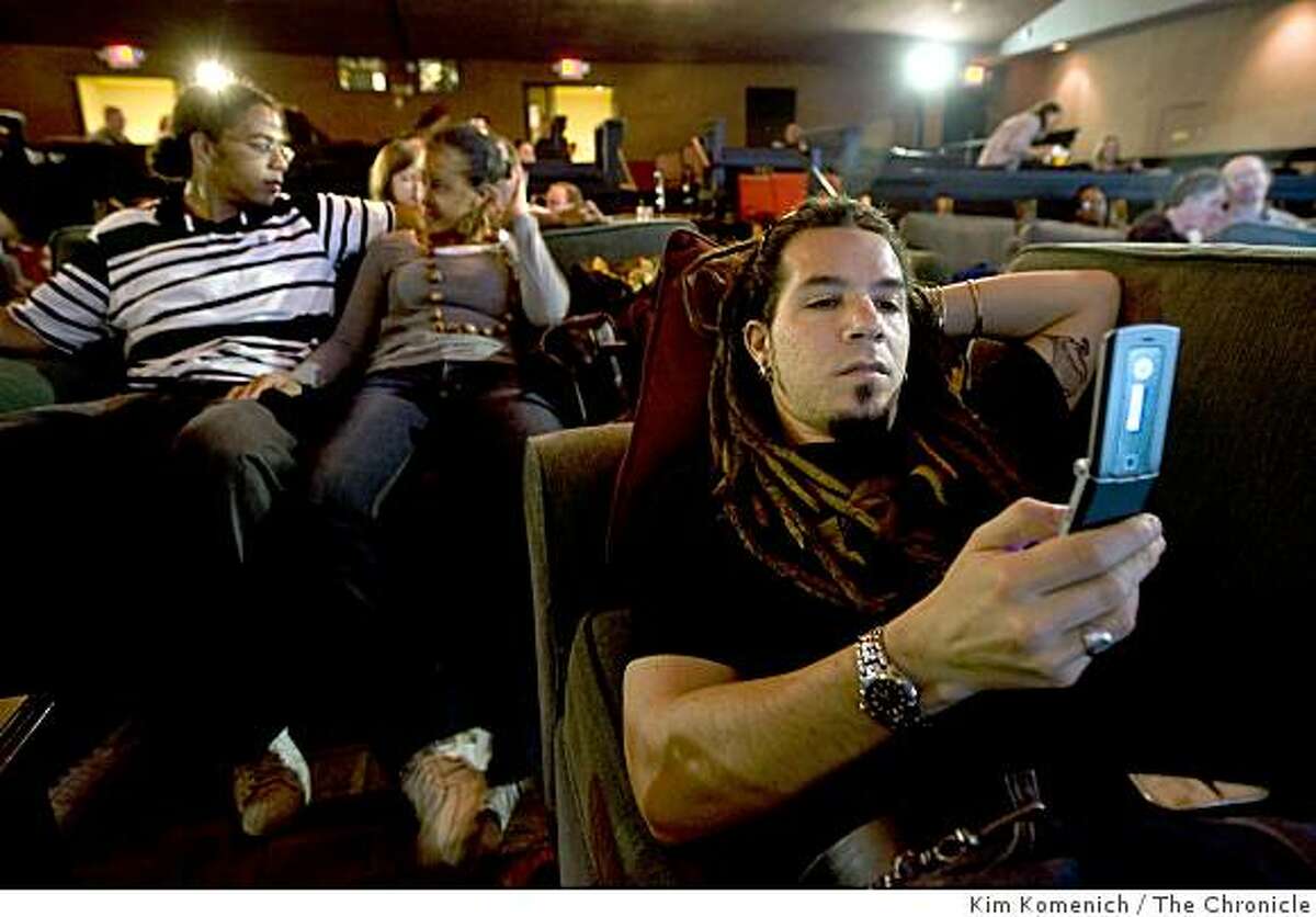 Seated in comfortable couches, Francisco Nanclares (R), texts a friend while Eric Wilkins of Walnut Creek, Calif., (L) and Maureen Akika of San Francisco, Calif., talk before the Parkway Speakeasy Theater in Oakland, Calif., shows "The Wrestler" on Thursday night, Mar. 19, 2009.
