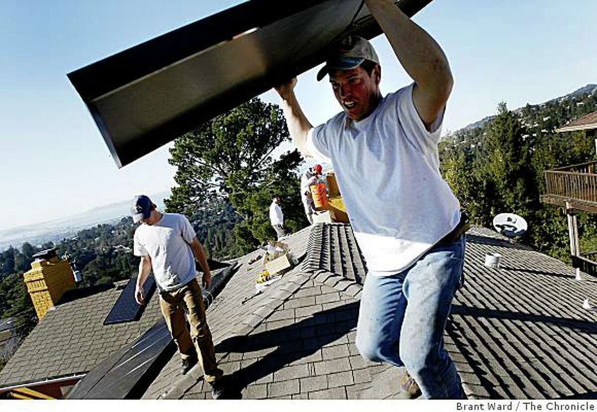 Solar installer Delmar Oliveira (right foreground) carried a panel to a new location on the roof. The solar industry has been a bright spot in a down economy. The Los Gatos based company Akeena Solar is installing 44 solar panels on a home in the Oakland hills Thursday January 15, 2008.