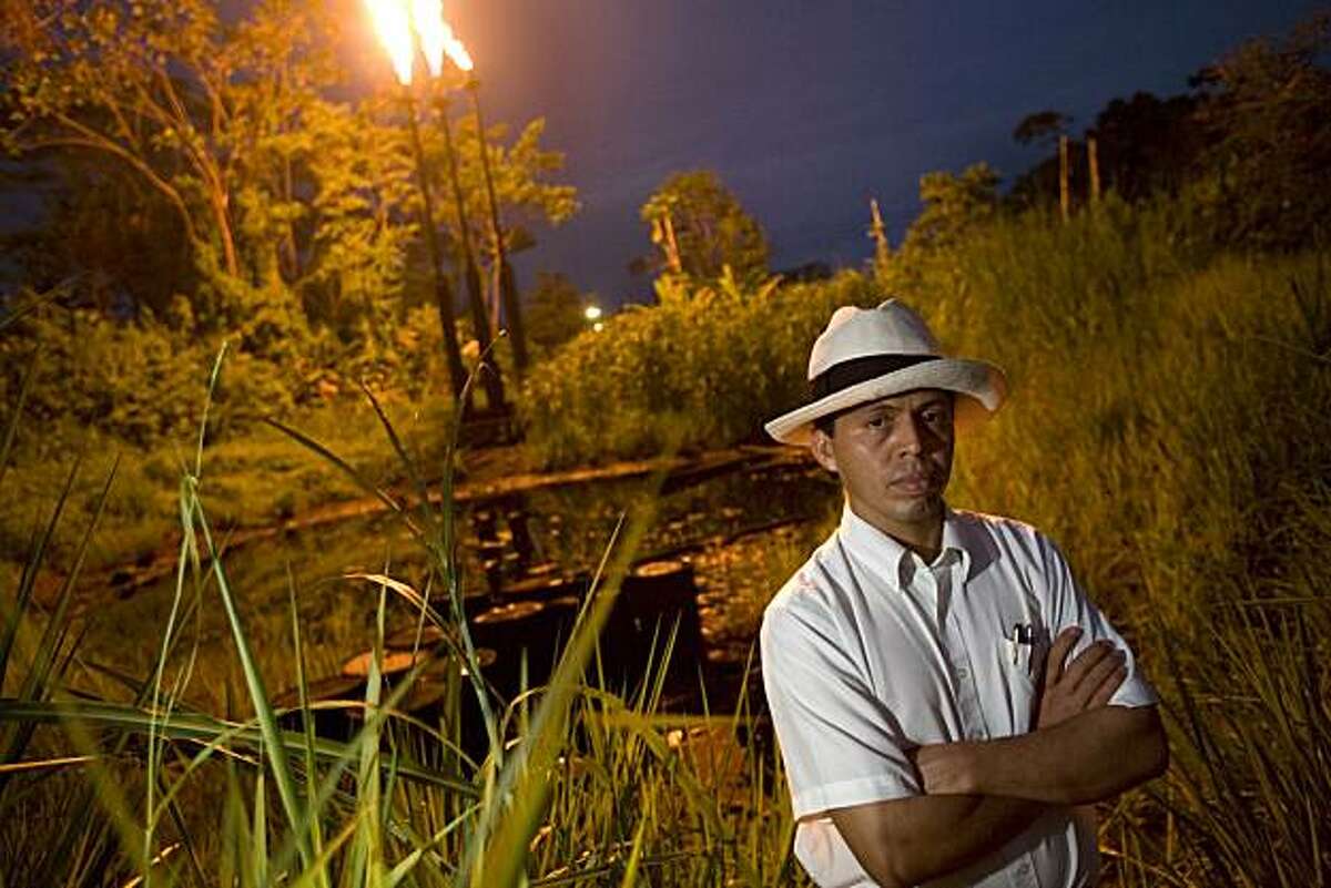 Pablo Fajardo stands in front of a pool of crude oil and waste and two towers that burn natural gas at the station North Lago Agrio in Lago Agrio, Ecuador, on December 17th, 2007. This pool of waste was left by Petro Ecuador, who took over after Texaco. Texaco passed on their bad practices to Petro Ecuador when they left the country. Pablo Fajardo is the lead attorney for the plaintiffs in the lawsuit against Texaco, which is now owned by Chevron. For twenty years Texaco was responsible for recklessly disposing of crude oil and toxic waste which leaked into the water supply of the people living in theses areas. There is now a higher rate of cancer, birth defects, and skin diseases. The 6 billion dollar case has been dragged out for 14 years. Pablo, who grew up in proverty and witnessed first hand the devastation brought to the people and environment because of the reckless behavior of Texaco, works on the case day and night. He just recently won the CNN Hero award in the category of fighting for justice, which has put the spotlight on the case that Chevron is is doing it's best to keep low profile. The six billion dollars that the people of the Ecuadorian jungle are asking of Texaco/Chevron would be used to clean up the the pools of crude oil which are still seeping into the environment. Photo by Ivan Kashinsky / Aurora Photos