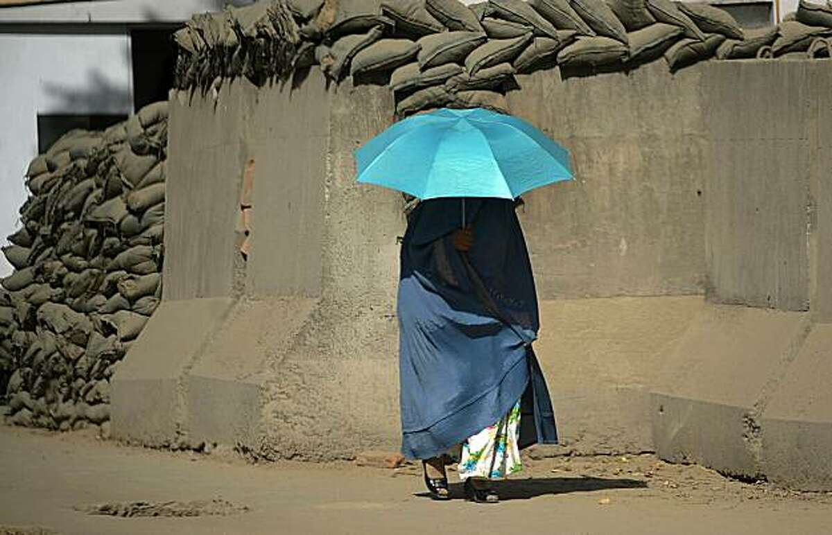 TOPSHOTS A burqa-clad Afghan woman uses an umbrella as she walks along a reinforced barrier in Kabul on August 23, 2010. Two NATO soldiers, one of them from the US, were killed in attacks in volatile regions of Afghanistan, the alliance said, a day afterfour US troops died in violence.
