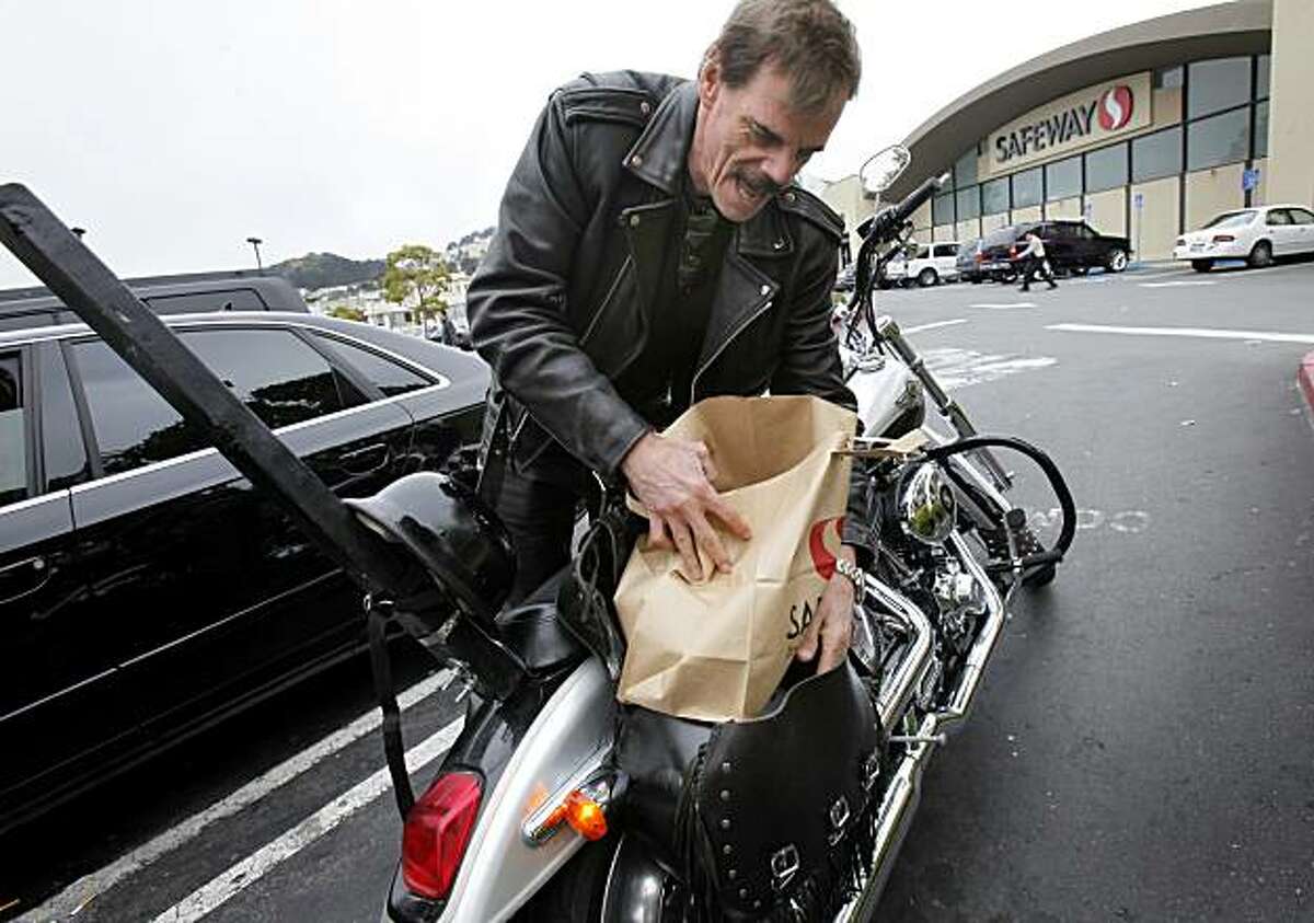 Ray Sayre loads his Harley Davidson with a paper bag after shopping at the Safeway store on Market Street Monday August 2, 2010. He thinks San Francisco makes it tough enough on motorcycles. San Francisco Supervisor Ross Mirkarimi and others want to begin charging shoppers for the use of paper and plastic bags.