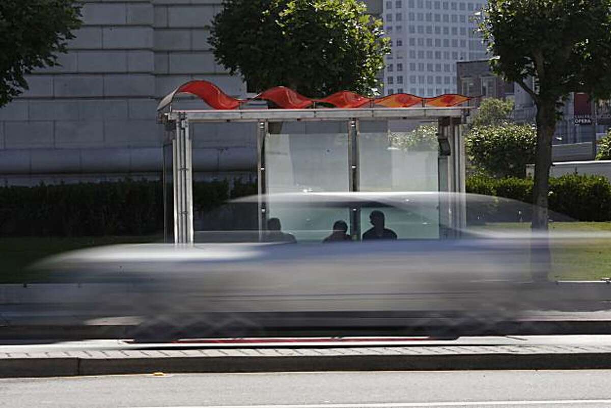 People wait for a bus at a bus shelter with a new roof as traffic passes by on Van Ness Avenue in San Francisco, Calif. on Wednesday July 14, 2010.