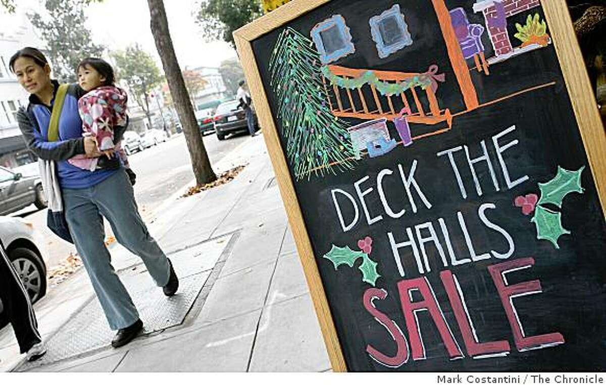 A man holding a child walks past a sale sign on College Ave. in the Rockridge district of Oakland, Calif. on Friday, November 28, 2008.