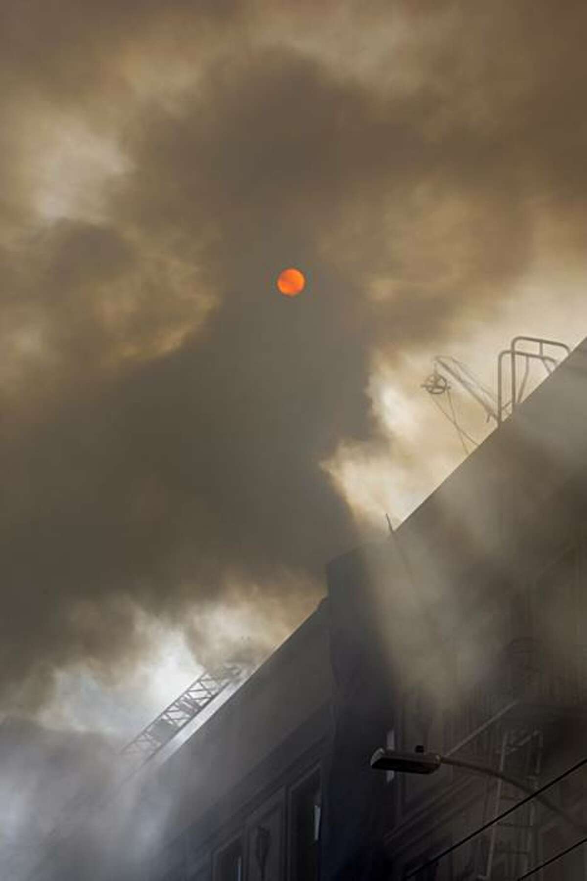 The sun peeks out through the smoke as San Francisco firefighters work on a structure fire at 111 Taylor St. on Thursday. The building is a halfway house for parolees.
