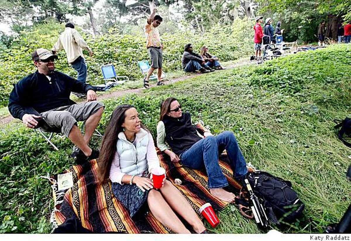 Kirk Sands, left, Dede Weadock, center, and Monique Laliberte, right, seated on the bank of Metson Lake outside the perimeter fence of the Outside Lands concert, listen to the music of Toots and the Maytals while Matt Zito and Greg Phillips play air guitar behind them, at the Outside Lands concert in Golden Gate Park in San Francisco, Calif. on Sunday, August 24, 2008.