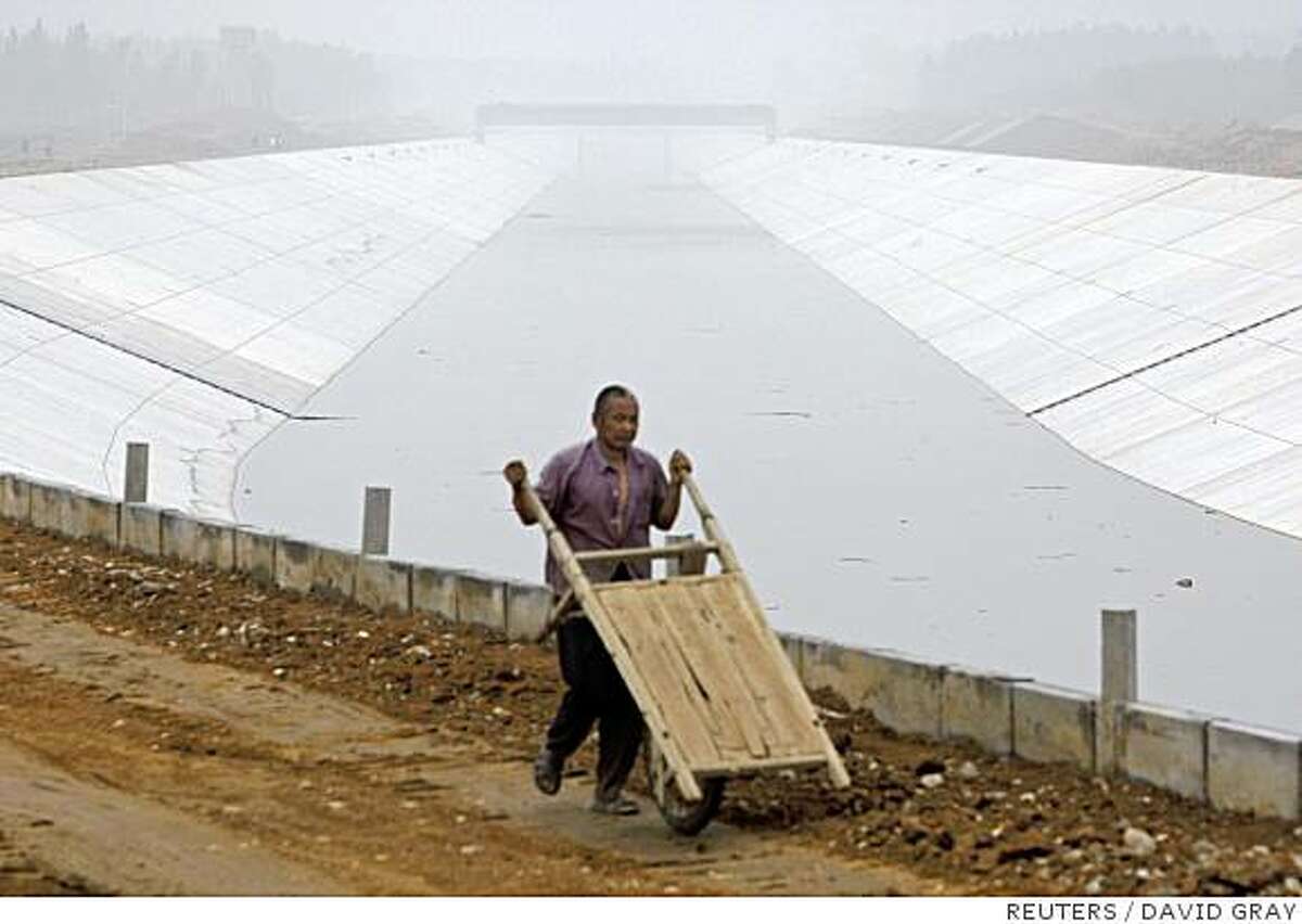 A worker pushes a cart along the banks of a section of the uncompleted Beijing-Shijiazhuang canal near the town of Baoding in Hebei Province, located around 120 kilometres (70 miles) south of Beijing June 25, 2008. The canal, part of the mammoth US$25 billion South-to-North Water Diversion scheme, aims to bring water from southern rivers to the arid north to bolster Beijing's scarce water supplies for the 2.5 million visitors expected during the 2008 Olympic Games. But China's ambitious hopes for a 'green' Olympics have magnified, not relieved, the city's reckless dependance on water for strained underground supplies and the mammoth canal project says Probe International, a Canada-based conservation group. Picture taken June 25, 2008. REUTERS/David Gray (CHINA)
