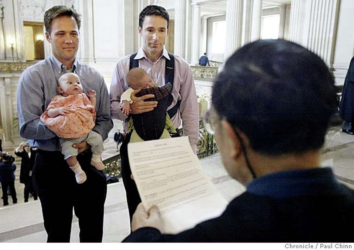 Eric Ethington (left) exchanges marriage vows with Doug Okun while holding their twin daughters, Sophia Rose and Elizabeth Ruby, in front of marriage commissioner Richard Ow at San Francisco City Hall.