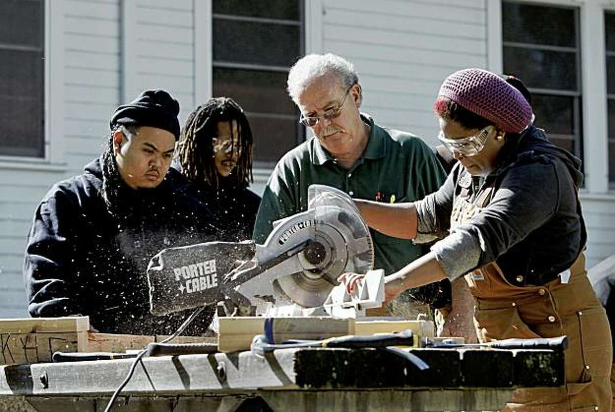 Under the watchful eye of Skills Instructor, Jeff McGallian, (right center) and fellow students, Julius Viclay, (left) and Antoine Hunter, (left center), Deanna Kelly, works the miter saw during a basic carpentry class at John Muir Charter School which works with at-risk youth providing educational and vocational programs, on Treasure Island in San Francisco, Calif. on Thursday October 22, 2009.