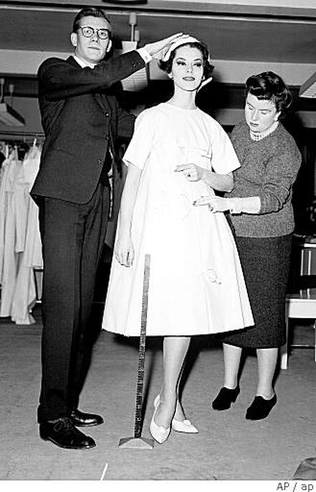 ** FILE ** In this March 14, 1958 file photo, working in front of a mirror, French fashion designer Yves Saint Laurent tries a hat on model Svetlana in his workshop in Paris, France. He is working on his Dior New York collection with the help of his assistant Marguerite Carre. The dress with narrow shoulders and wide, swinging skirt is designed in the trapeze line, which Saint Laurent introduced in his first solo collection in February. Yves Saint Laurent, who reworked the rules of fashion by putting women into elegant pantsuits that came to define how modern women dressed, died Sunday evening June 1, 2008. He was 71. (AP Photo/File)
