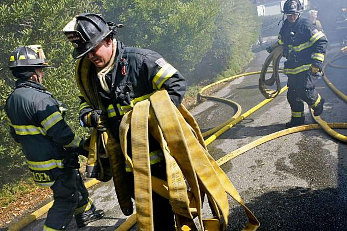 Marin County Firefighters Peter Falk (center) gathers up the hoses after cleaning up after a four alarm fire that broke out around 9:30 am at 116 Lyford Drive, Wednesday Oct. 21, 2009, in Tiburon, Calif.