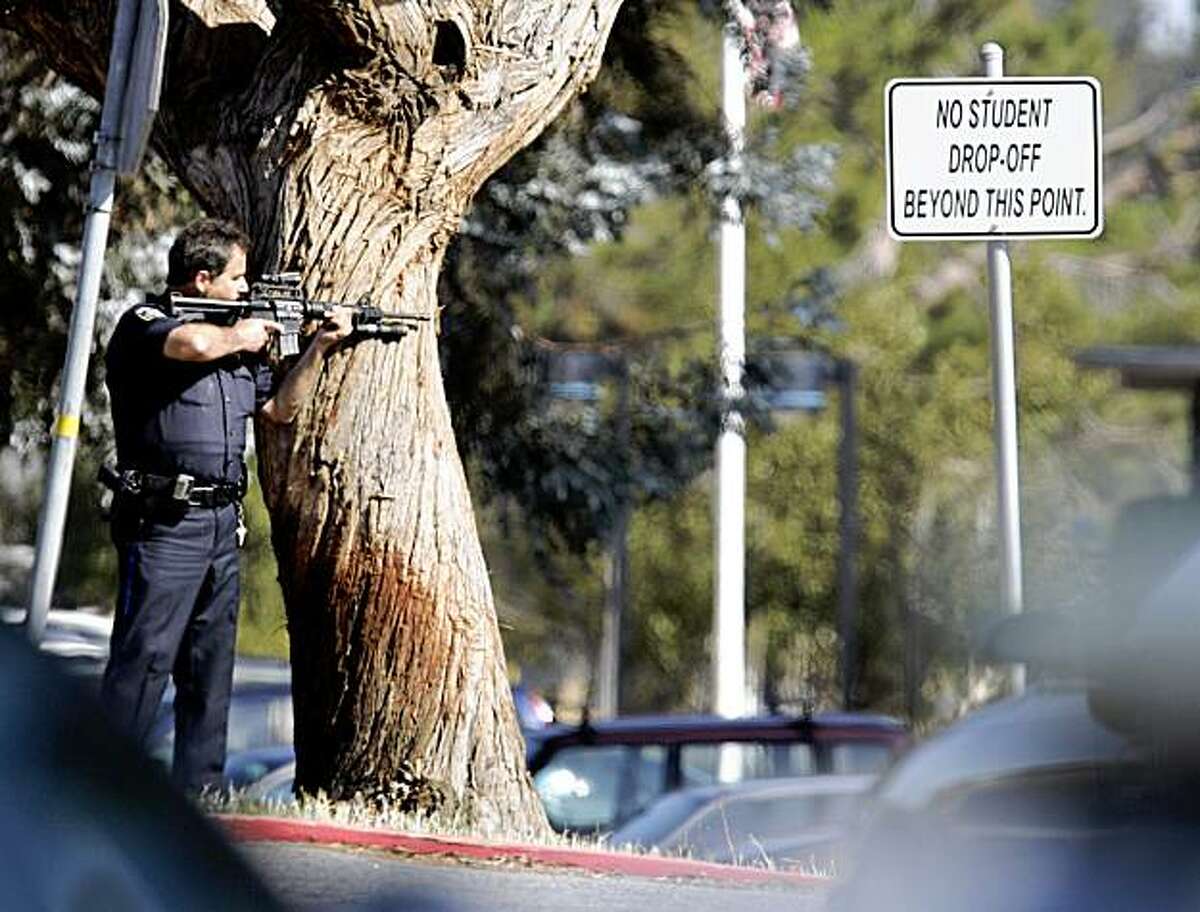 A police officer points his weapon towards Hillsdale High School in San Mateo, Calif., Monday, Aug. 24, 2009. Authorities say an explosion at this high school has forced evacuation of students and cancellation of classes. There are no reports of injuries. San Mateo police Lt. Mike Brunicardi says officers received several calls just after 8 a.m. Monday from teachers and staff reporting some kind of blast at the high school. (AP Photo/Paul Sakuma)
