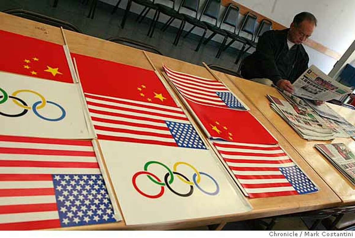 Sik Hoi Wong reads a newspaper as Chinese, American and Olympic flags lay on a table at the Chinese American Association of Commerce on Clay St. in the Chinatown district of San Francisco, Calif. on April 3 ,2008. Photo by Mark Costantini / San Francisco Chronicle. Ran on: 04-06-2008 Chinese, American and Olympic flags show pride at the Chinese American Association of Commerce.